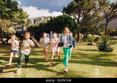 Un groupe d'enfants joyeux courant joyeusement ensemble sur l'herbe sous un ciel dégagé. Parfait pour représenter le plaisir en plein air, la joie de l'enfance, et liv dynamique Banque D'Images