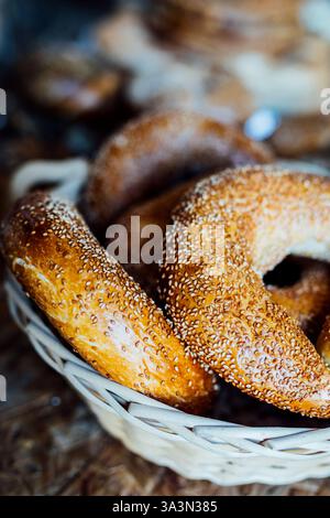 Gros plan de bagels au sésame fraîchement cuits disposés dans un panier traditionnel en osier. La croûte brun doré est généreusement saupoudrée de graines de sésame, c Banque D'Images