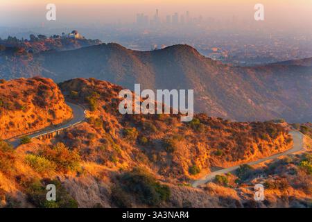 Des chemins de randonnée sinueux dans Griffith Park mènent à l'observatoire Griffith surplombant le centre-ville brumeux de Los Angeles, avec des collines baignées de lumière chaude du soleil. Banque D'Images