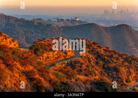 Vue panoramique sur les chemins de randonnée sinueux dans Griffith Park menant à l'observatoire Griffith, surplombant le centre-ville brumeux de Los Angeles au coucher du soleil. Banque D'Images