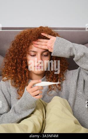 Une femme malade est allongée dans son lit et vérifie sa température corporelle Banque D'Images