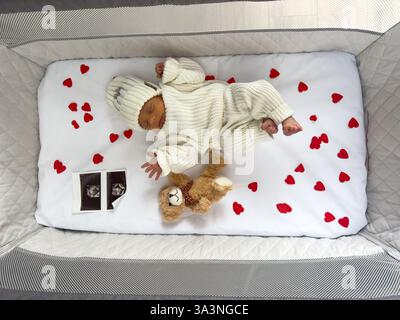 Bébé nouveau-né dormant dans un berceau avec des coeurs et un ours en peluche Banque D'Images