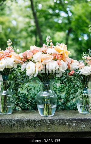 Gros plan d'élégantes pêches et bouquets de mariage blancs dans des vases en verre. Banque D'Images