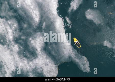 Yellow paddleboard (SUP) coupant dans les eaux glacées sur un lac gelé Banque D'Images