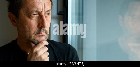 Homme adulte adulte caucasien sérieux regardant par la fenêtre et la pensée, foyer sélectif Banque D'Images