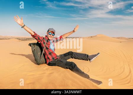Backpacker assis sur une vaste dune de sable, se sentir libre à bras ouverts, embrassant la beauté du paysage désertique Banque D'Images