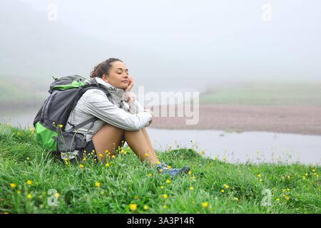 Trekker assis sur l'herbe reposant dans la montagne avec les yeux fermés Banque D'Images