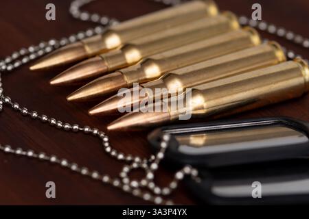 Munitions et jetons - un symbole du service militaire cinq munitions de fusil alignées dans une rangée et des étiquettes de chien de l'armée sur une chaîne couchée sur un fond sombre. Banque D'Images