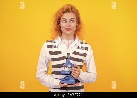 Une femme professeur de biologie scolaire tient un microscope. Femme professeur de biologie. Professeur avec microscope isolé sur jaune. Sciences biologiques pour la femme Banque D'Images
