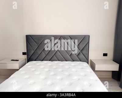 une chambre moderne au design minimaliste, avec une tête de lit rembourrée grise avec un motif géométrique Banque D'Images