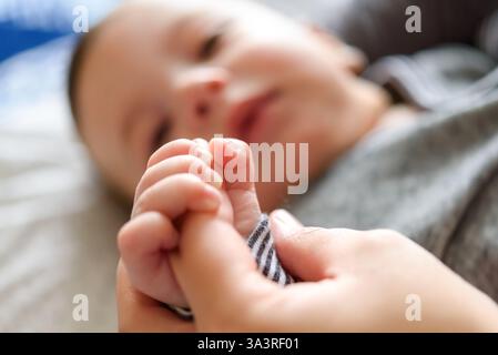 Bébé garçon allongé et tenant son doigt de mère Banque D'Images