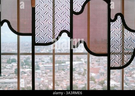 Une vue détaillée à travers un écran décoratif révèle un paysage urbain. L'écran présente des motifs géométriques et des textures de rotin. La conception fournit un Uni Banque D'Images