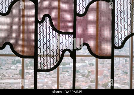 Une cloison en treillis de conception complexe, composée de rotin et d'éléments géométriques à motifs, filtre la lumière et encadre un paysage urbain tentaculaire. Banque D'Images