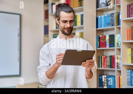 Jeune homme beau utilisant la tablette numérique à l'intérieur du bureau de bibliothèque Banque D'Images