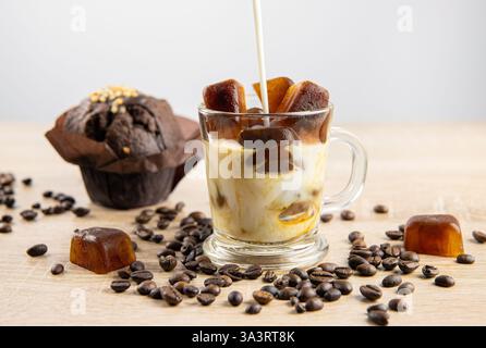 Vue de côté de la boisson au café glacé, verser le lait, glaçons au café dispersés sur la table, décorés avec des grains de café. Prise de vue en studio. Concept de glace de café. Banque D'Images