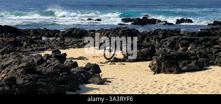 Une bicyclette solitaire appuyée contre des roches volcaniques au bord de la mer, Fuerteventura, îles Canaries, Espagne, Europe, UE Banque D'Images