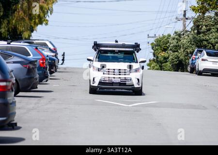 Amazon Zoox Toyota Highlander équipé de la technologie de conduite autonome navigue dans une rue en pente bordée de voitures garées dans un quartier résidentiel. Vue de face Banque D'Images