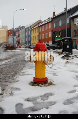 Bouche d'incendie rouge et jaune située à Laugavegur Reykjavik Islande entourée de sentiers enneigés et de bâtiments de la ville. Banque D'Images
