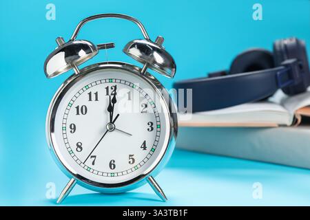 Réveil, livres et écouteurs sur fond bleu clair Banque D'Images