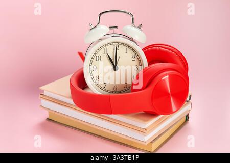 Réveil, livres et écouteurs sur fond rose clair Banque D'Images