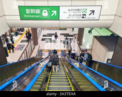 Un escalier roulant descendant à une gare avec des passagers et un panneau indiquant les trains Shinkansen. Banque D'Images