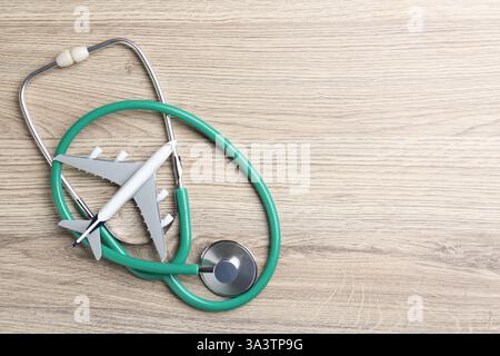 Tourisme médical. Stéthoscope et modèle d'avion sur fond de bois clair, vue de dessus. Espace pour le texte Banque D'Images