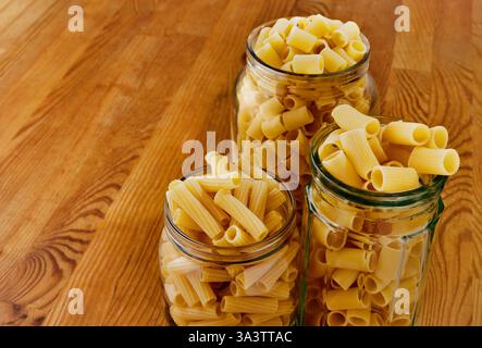 Variété de formes de pâtes italiennes, tortiglioni et rigatoni dans un pot en verre sur une table en bois, morceaux tubulaires de pâtes sillonnées faites avec du blé dur s. Banque D'Images