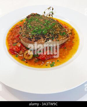 Steak de thon poêlé en croûte de graines de sésame noir dans une sauce tomate rôtie avec des olives vertes. Banque D'Images