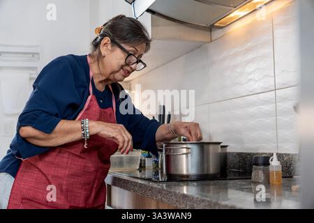 Heureuse femme retraitée ajoutant des épices à la casserole sur le poêle Banque D'Images