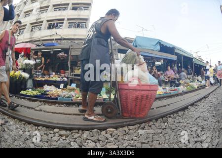 Le mâle asiatique pousse les légumes et les articles dans un panier en plastique sur un camion à main à la gare de Mahachai. Banque D'Images