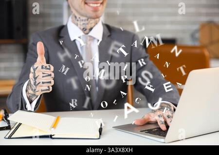 Homme d'affaires heureux avec ordinateur portable et lettres volantes montrant un geste pouce vers le haut dans le bureau Banque D'Images