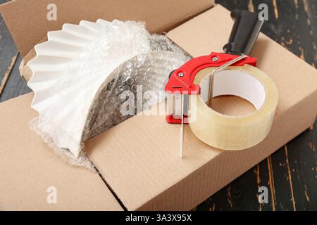 Distributeur de ruban d'emballage et boîte en carton sur fond en bois noir Banque D'Images