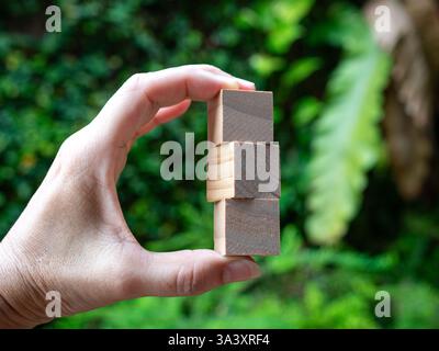 Main tenant trois blocs de bois. Fond vert de nature. Banque D'Images
