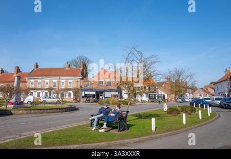 Couple parlant assis sur un banc en bois sur un bord d'herbe dans la place du marché dans le North Yorkshire ville de marché d'Easingwold. Banque D'Images