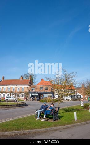 Couple parlant assis sur un banc en bois sur un bord d'herbe dans la place du marché dans le North Yorkshire ville de marché d'Easingwold. Banque D'Images