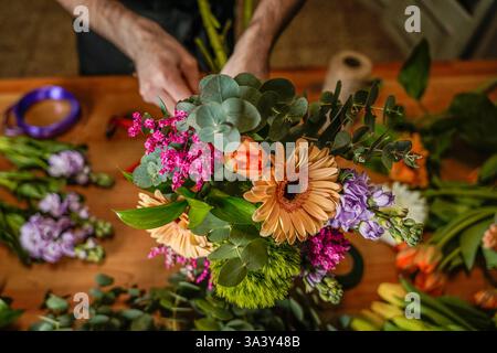 Fleuriste créant un bouquet vibrant avec des marguerites gerbera, eucalyptus et diverses fleurs colorées Banque D'Images