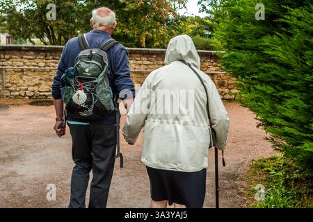 Un couple âgé marche main dans la main le long du chemin de gravier vers la chapelle de Sainte-Bernadette au couvent Saint-Gildard sur la rue du même nom, Rue Saint-Gildard, à Nevers, Bourgogne-Franche-Comté, France. Une coquille saint-Jacques sur le sac à dos de l'homme le marque comme un pèlerin. Bernadette Soubirous, qui a vécu les apparitions mariales à Lourdes en 1858, est entrée dans le couvent en 1866 et y est morte en 1879 à l'âge de 35 ans. Son corps, trouvé largement incorrompu lors des exhumations en 1909, 1919 et 1925, repose dans une reliquaire vitrée dans la chapelle du couvent depuis 1925 – toujours un important lieu de pèlerinage Banque D'Images