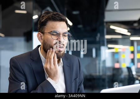 Homme souffrant de maux de dents sur le lieu de travail à l'intérieur du bureau. Homme d'affaires travaillant sur le lieu de travail malade a l'inflammation des gencives. Banque D'Images