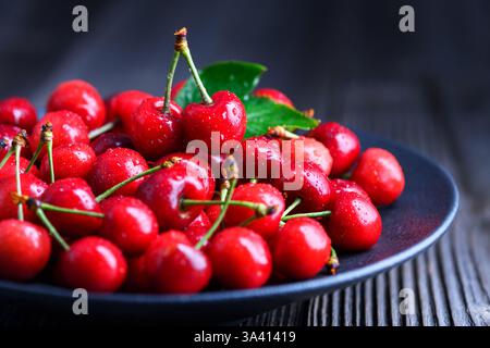 Juste cueilli et lavé des cerises mûres dans une plaque noire sur une table en bois rustique. Photographie culinaire Banque D'Images