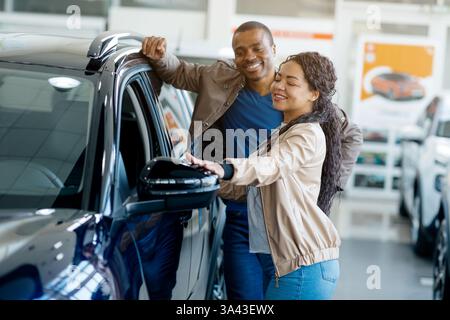 Heureux couple afro-américain appréciant leur expérience d'achat de voiture dans un concessionnaire tout en discutant des caractéristiques et des options Banque D'Images