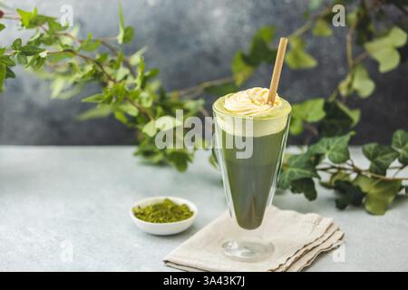 Préparation d'un latte matcha glacé garni de crème fouettée et garni de branches de lierre fraîches, créant une boisson rafraîchissante d'été Banque D'Images