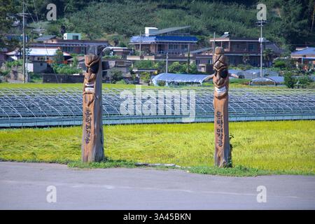 Ville de Gwangyang, Corée du Sud - 3 octobre 2021 : une paire de mâts totémiques traditionnels de Jangseung se tient à l'entrée d'un village rural, entouré de RIC Banque D'Images