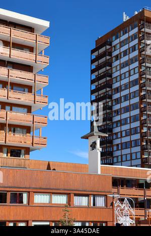 Une photographie d'immeubles modernes en bois avec balcons, placés contre un ciel bleu clair. Un petit clocher blanc avec un toit escarpé se dresse en t Banque D'Images