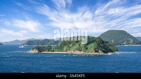 Petite île japonaise couverte d'arbres avec phare blanc sur le passage à Hiroshima, vue de la mer près de la baie d'Hiroshima, Japon le 29 septembre 2024 Banque D'Images