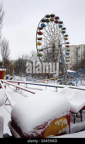 Parc d'attractions abandonné. Vieille grande roue rouillée et montagnes russes couvertes de neige, scène sombre, fantôme et carrousel vide sans personne pour enterta Banque D'Images