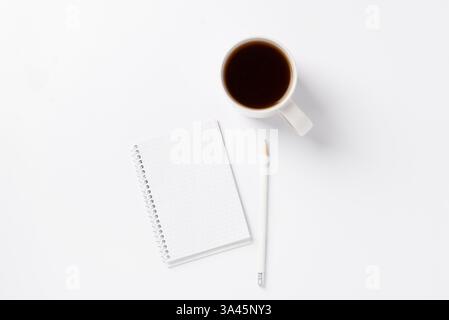 Cahier, crayon et tasse blanche avec café noir sur fond blanc. Concept de propreté. Fond monochrome blanc avec ordinateur portable Banque D'Images