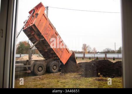 Une grande remorque verse du sol sur un chantier de construction en Ukraine, avec un camion et de l'équipement lourd en arrière-plan. construction, aménagement du territoire, ex. Banque D'Images