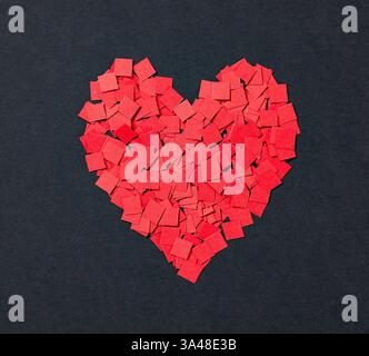 signe en forme de coeur fabriqué à partir de petits morceaux de carrés de papier appliqué de couleur rouge. Fond de papier noir Banque D'Images
