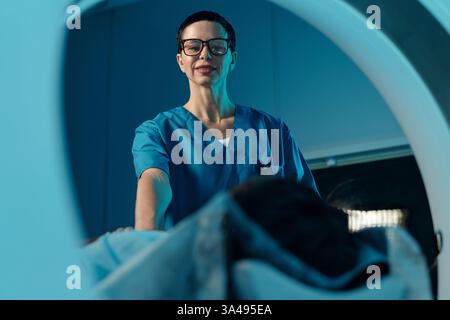 Professionnel de santé en gommage bleu aidant le patient en milieu hospitalier. La personne porte des lunettes et semble réfléchie tout en fournissant des soins pour le bien-être du patient Banque D'Images