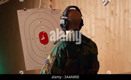 Le personnel militaire heureux dans le champ de tir tire des cibles avec une arme de poing, satisfait après avoir obtenu un résultat positif. Joyeux soldat de formation avec arme à feu exulte après avoir frappé avec précision Bullseye, caméra B. Banque D'Images